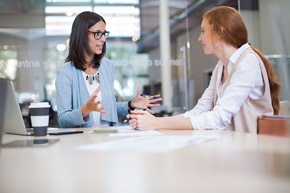 Two seated professionally dressed females mid discussion