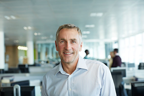 A casually dressed man, standing in an office smiling